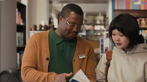 Un employé de librairie recommande un livre à un jeune client en sweat à capuche