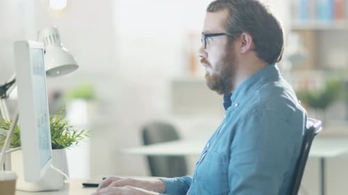 Close-up of a Young Bearded Man Working on Personal Computer in His Light and Modern Office.