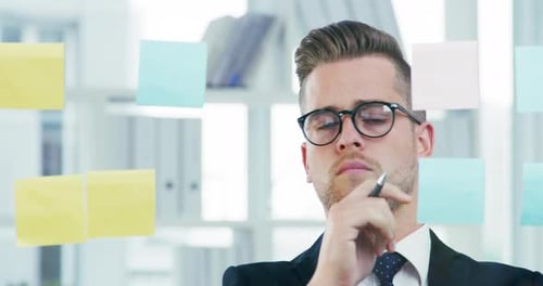 4k video footage of a young businessman writing notes on a glass wall in an office