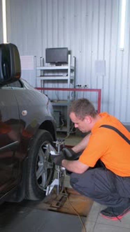 A Man is Fixing a Vehicle in a Garage with Automotive Tire Wheel and Lighting Vertical Video