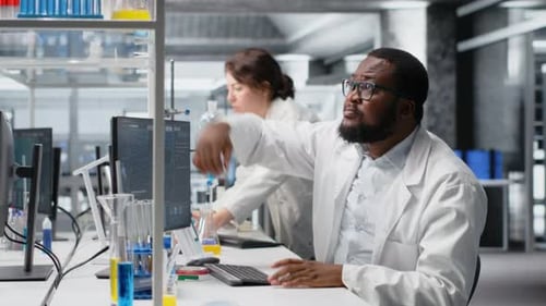 Clinical Microbiologist in Lab Looking at Blood Sample in Test Tube Using PC