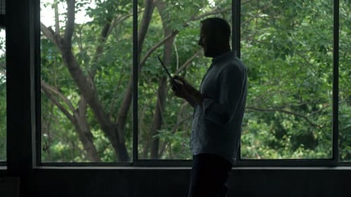 Man Using Tablet by Large Window with Green Trees