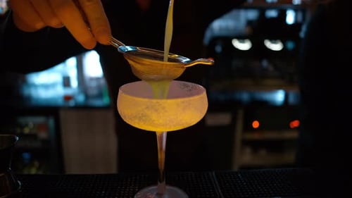 Barman pouring green alcohol cocktail on a bar with neon lights at night