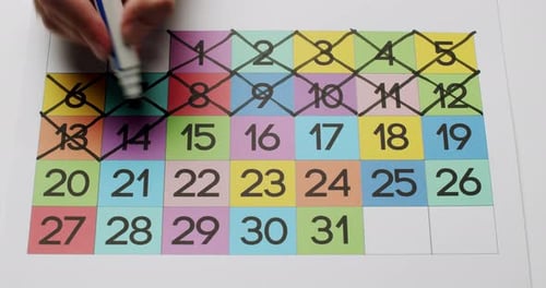 Hand Marking Days on a Colorful Monthly Calendar with Marker