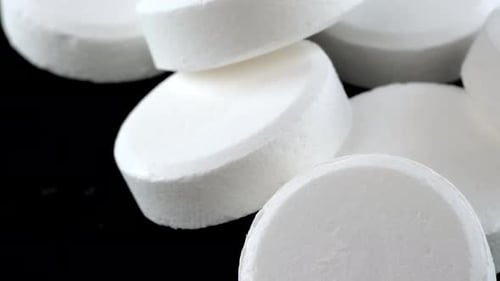 Heap white round pills lying on black table tracking shot, close-up. Medical care and health.