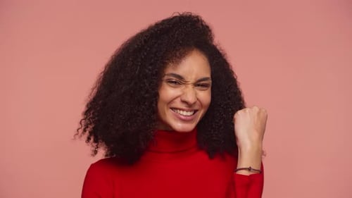 Excited Woman Celebrating Success with Fist Pump on Pink Background
