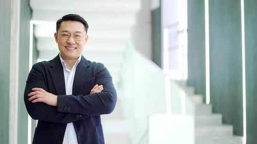 Portrait of a smiling Asian businessman in a formal suit standing in a modern office building. Happy