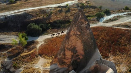 Flying past rock formation to reveal horse riders traveling the wild of Turkey at sunset