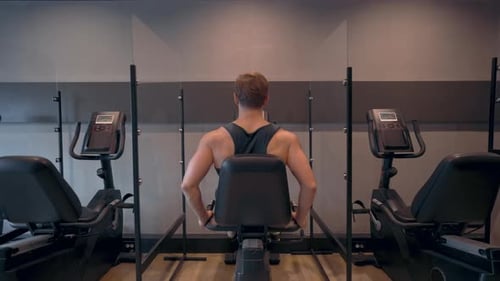 Rear view of Athletic Man Doing Cardio Cycling Training in Stationary Bicycle at Gym