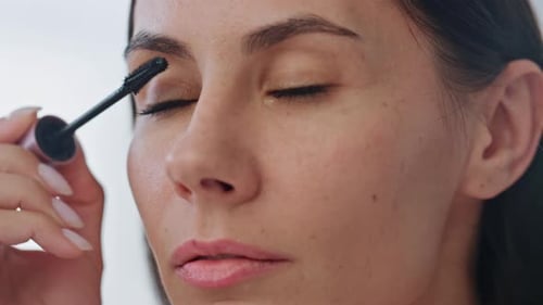 Serious Model Applying Mascara Indoors Closeup. Focused Lady Face Looking Mirror Holding