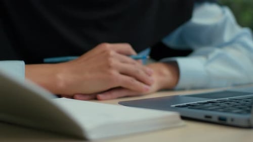 Hands Holding Pen Above Notebook on Desk