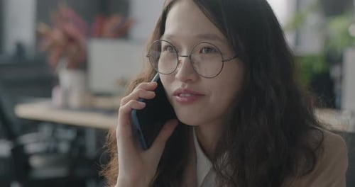 Young Asian Woman Employee Speaking on Mobile Phone Discussing Business Cooperation in Office