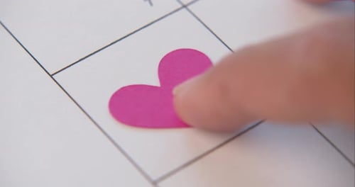 Single pretty pink heart being pushed into the 14th square on a calendar. Valentines Day.