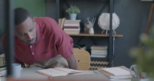African American Man Coming to Office Sitting Down at Desk and Working with Laptop Computer