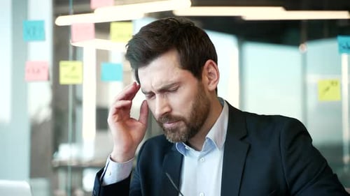 Businessman suffering from headache while sitting at workplace in business office. Tired man worker