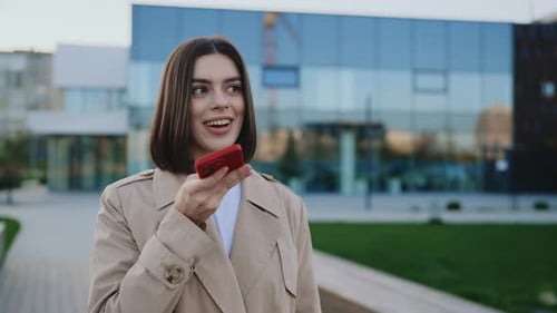 Charming Girl Recording Voice Message on Smartphone Outdoors Near the Local Lake Attractive Business