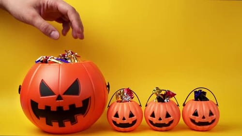 Halloween candy in pumpkin buckets on yellow background