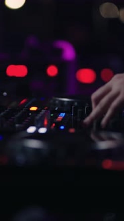 Nahaufnahme eines DJ-Mischpults mit bunten Lichtern und verschwommenen Händen, die die Bedienelemente im Dunkeln einstellen