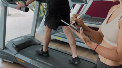 Man Walks Treadmill While Woman Takes Notes on Tablet