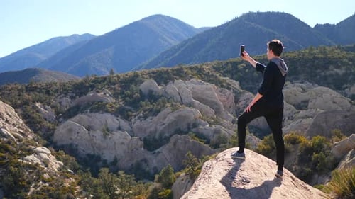 A handsome millennial man taking smartphone photos for social media on a mountain peak hike in the C