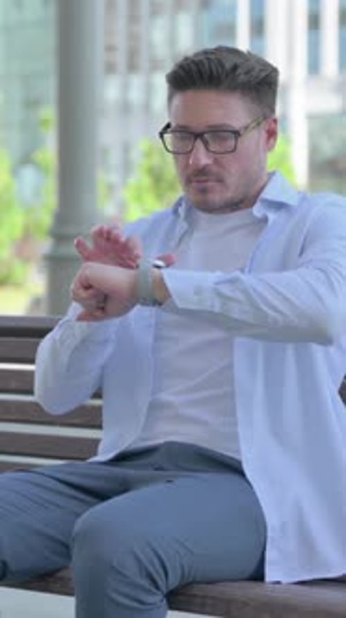 Man Sitting on Bench Uses Smartwatch in City