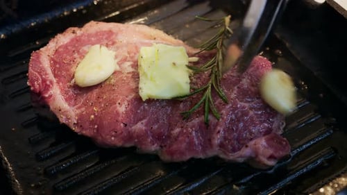 Close up of butter melting over a steak with garlic and rosemary in a hot grill pan