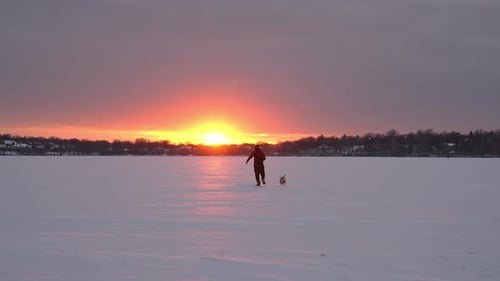 Man a Dog Walking on Frozen Lake at Sunset