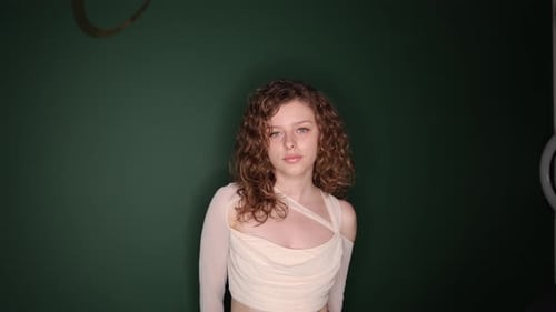 A Stylish Model Poses Gracefully with Curly Hair in an Elegant Outfit Against a Vibrant Green