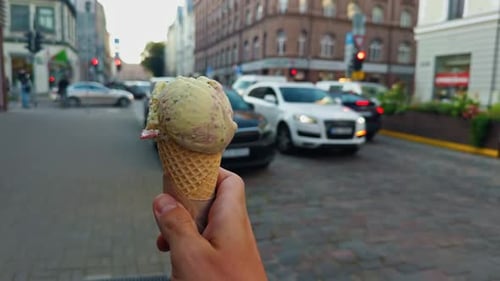 A Hand Gripping a Delicious Ice Cream Cone While Strolling Along a Bustling City Street on a Sunny