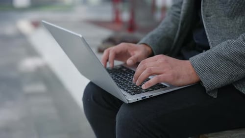 Kaukasischer Geschäftsmann, Benutzerhand, tippt auf Laptop-Tastatur, sitzt auf der Bank Geschäftsmann