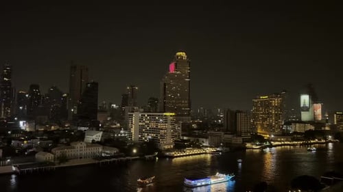 Nighttime riverside view of Bangkok with illuminated boats and modern skyscrapers on the riverbank