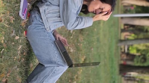 Young Woman with a Laptop Sitting on the Grass in the Park on an Autumn Day Vertical Video