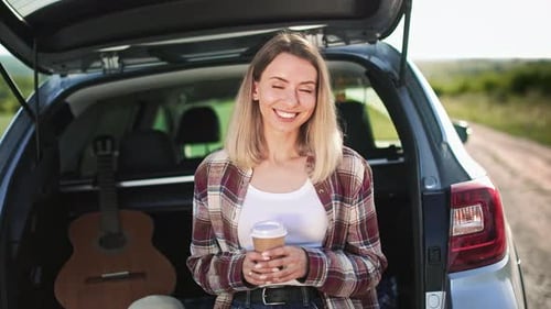 Cheerful Woman Sitting in Car Trunk Looking at Camera Smiling