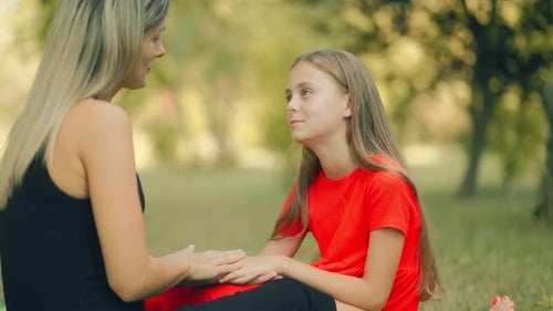 Loving Mom and Daughter Chatting on a Park Blanket in the Sunshine