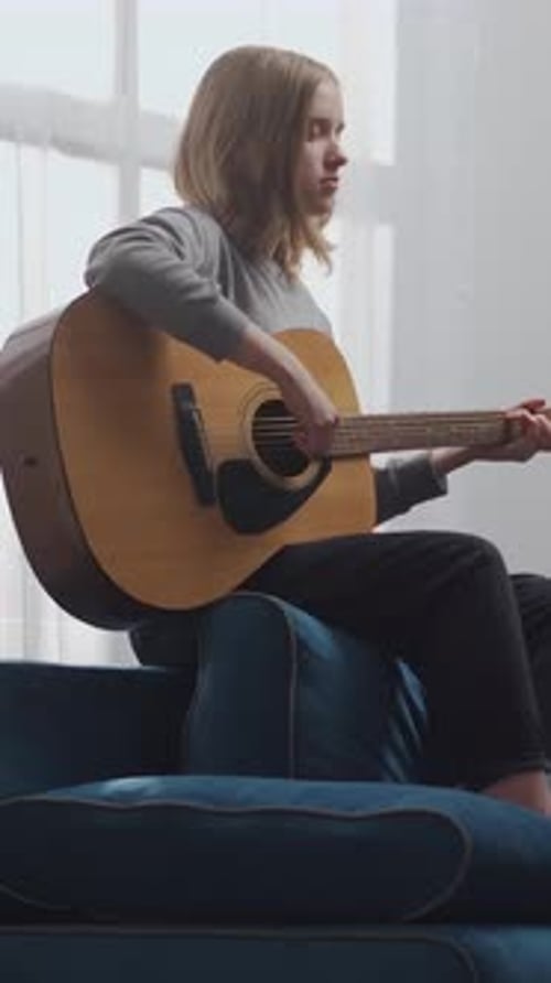 Teen Girl Playing Acoustic Guitar on Blue Couch