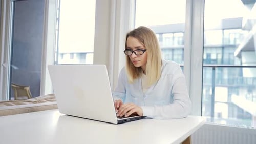 Portrait young female freelancer working on laptop or computer at home at a modern office desk.