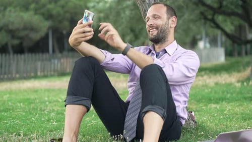Businessman Taking Selfie Photo with Cellphone Sitting on Grass in Park 30s