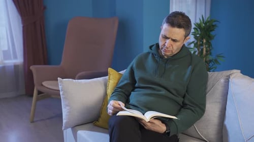 The man is reading a book on the sofa at home. learning, reading book, resting at home concept.