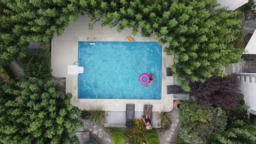 Young couple enjoying summer by the pool - he jumps into the water and they lie on sun lounger - dro