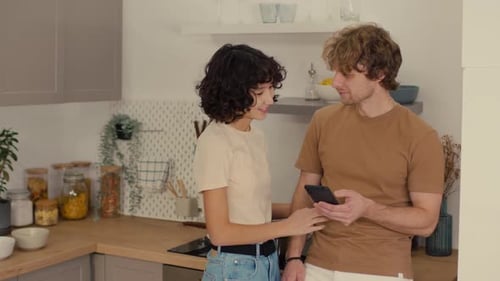 Affectionate Couple Using Phone Together in Kitchen