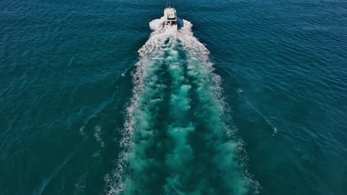 Long white wake trail of speedboat cruising over calm blue sea water. Aerial backward tilt-up reveal