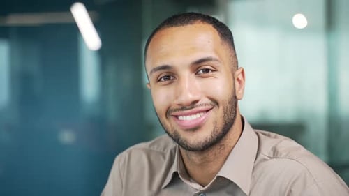 Close up portrait of a young adult man in a shirt smiling and looking at the camera while sitting