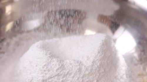 close up of sifting white flour or sugar powdered with sieve in steel bowl for pie, french dessert