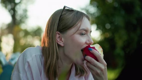 Close Up of Smiling Lady Taking a Bite From Red Apple Outdoors