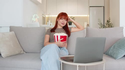 Une jeune femme avec du pop-corn regarde la bande-annonce du film sur un ordinateur portable rit à haute voix et profite d'un teaser amusant et de l'encourager
