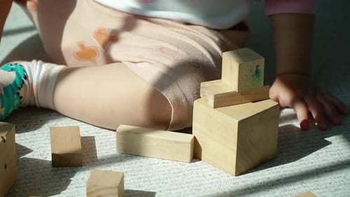 Hands of baby learning by stacking up and balancing wooden blocks - caucasian baby girl playing