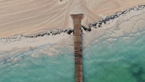 AERIAL DIRECTLY ABOVE Wooden Jetty With Clear Water Lapping At Sandy Beach