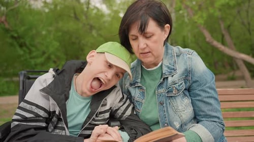 Woman Reading Book to Young Man in Wheelchair