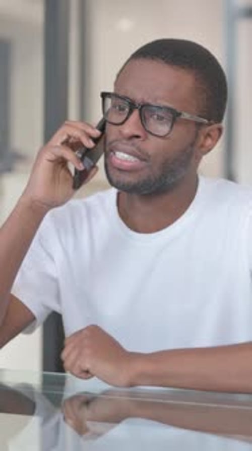 Young Man Talking on the Phone at Desk Indoors