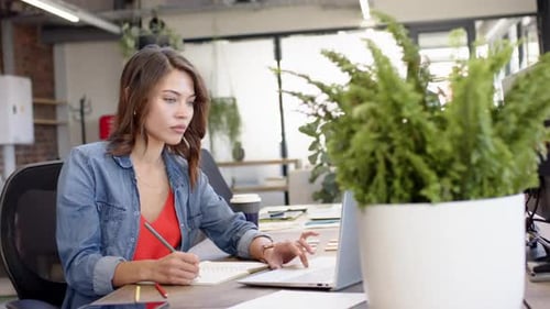 Working in office, woman using laptop and taking notes, focusing on work